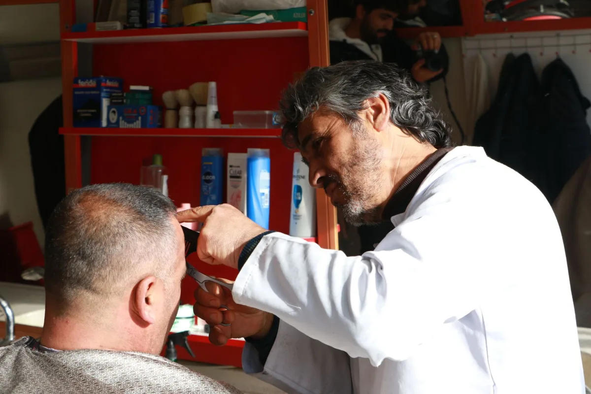 Barbeiro corta o cabelo de cliente sentado na cadeira de uma barbearia bem equipada