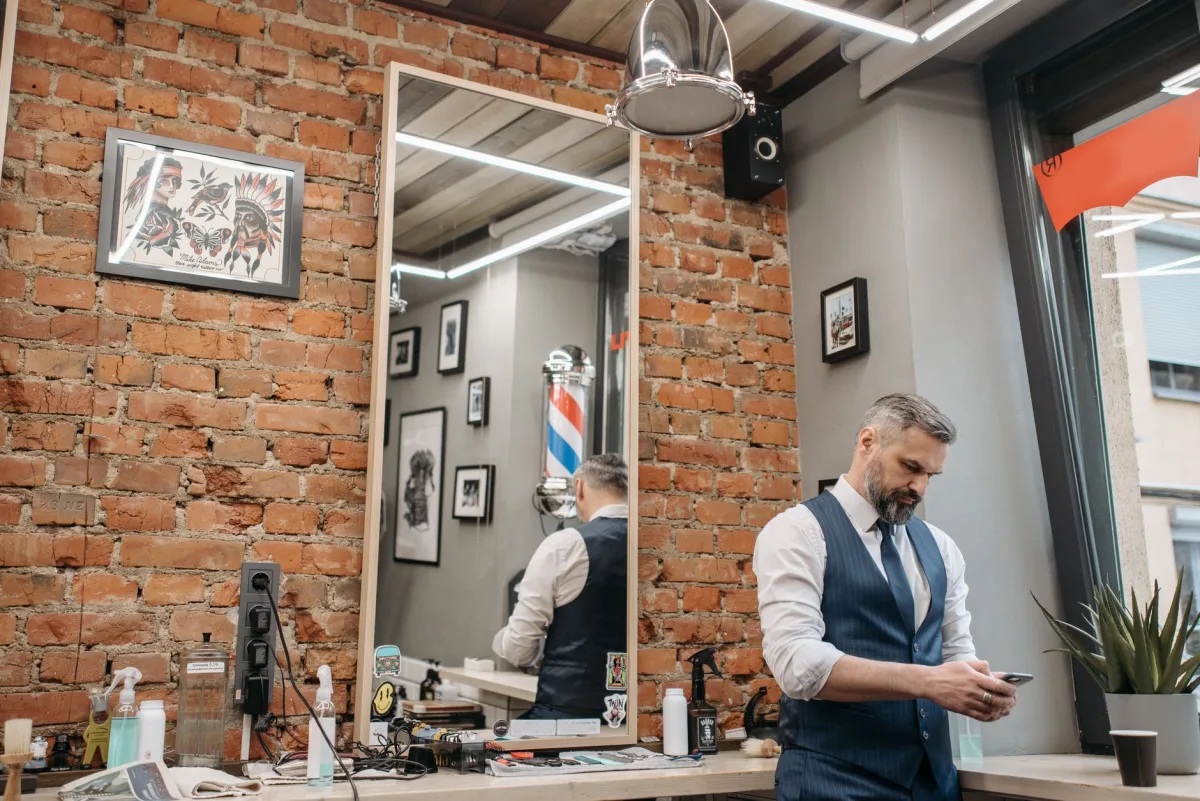 Barbeiro usando o celular dentro de uma barbearia moderna com parede de tijolos