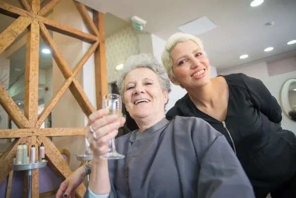 Cabeleireira e cliente idosa sorrindo juntas em um salão de beleza