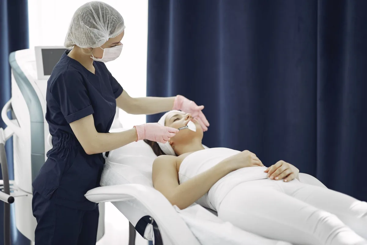 Esteticista aplica tratamento facial em cliente deitada em maca de clínica de estética