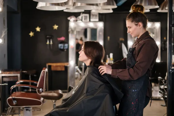 Cabeleireira ajeita o cabelo de cliente sentada em salão de beleza, com cadeira vazia ao lado